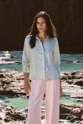 Mae Satin Shirt in mint worn front on with pink wide-leg trousers, coastal rocks behind