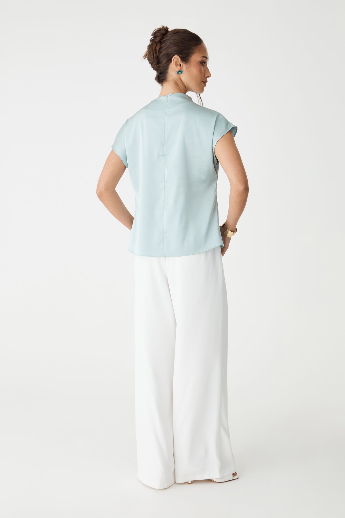 Back view of the pale blue Zafina Pleated Draped Top with invisible back zipper, worn with white trousers