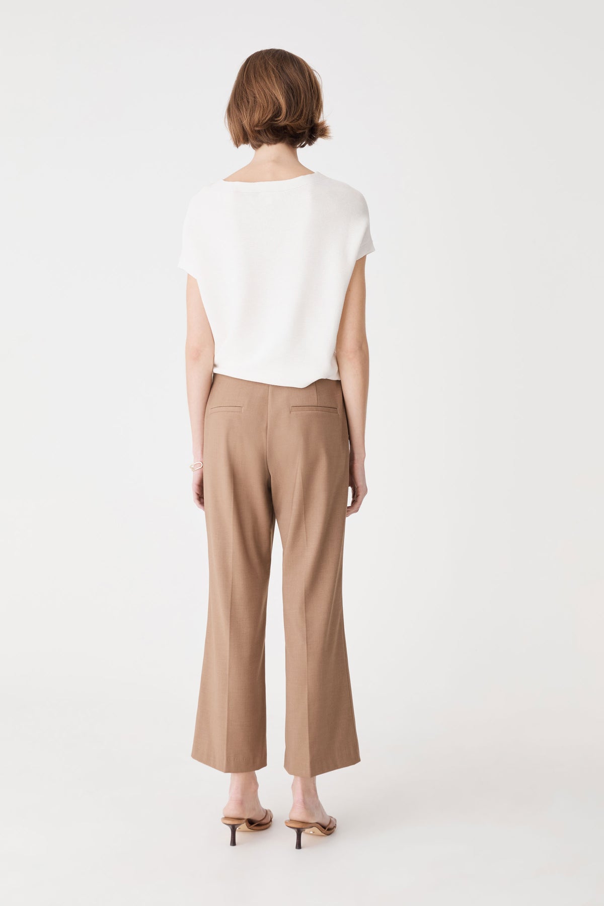 Back view of the ivory knit top with tan trousers, showing boxy shape and ribbed hem band