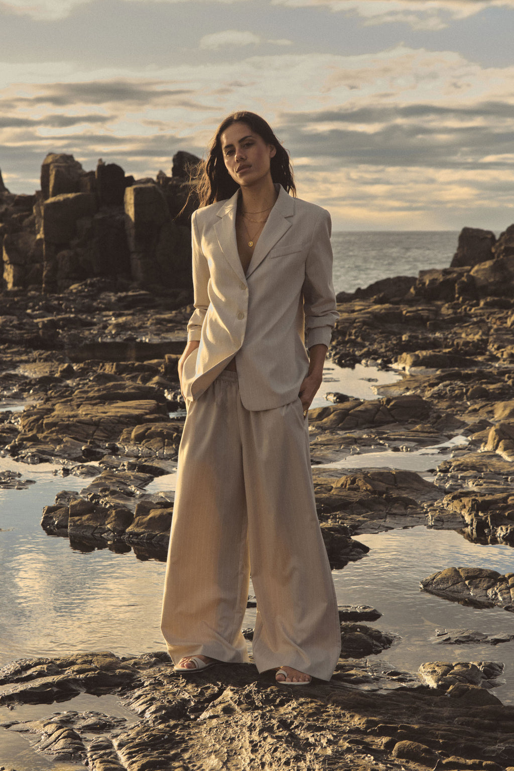 Zoe Elastic Pinstripe Pants in beige pinstripe worn on rocks with a matching blazer, full-length front view