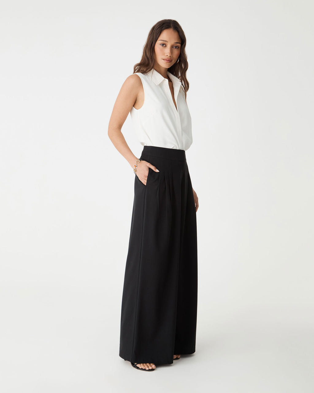 Side view of the ivory Brooklyn Sleeveless Shirt with black wide-leg trousers