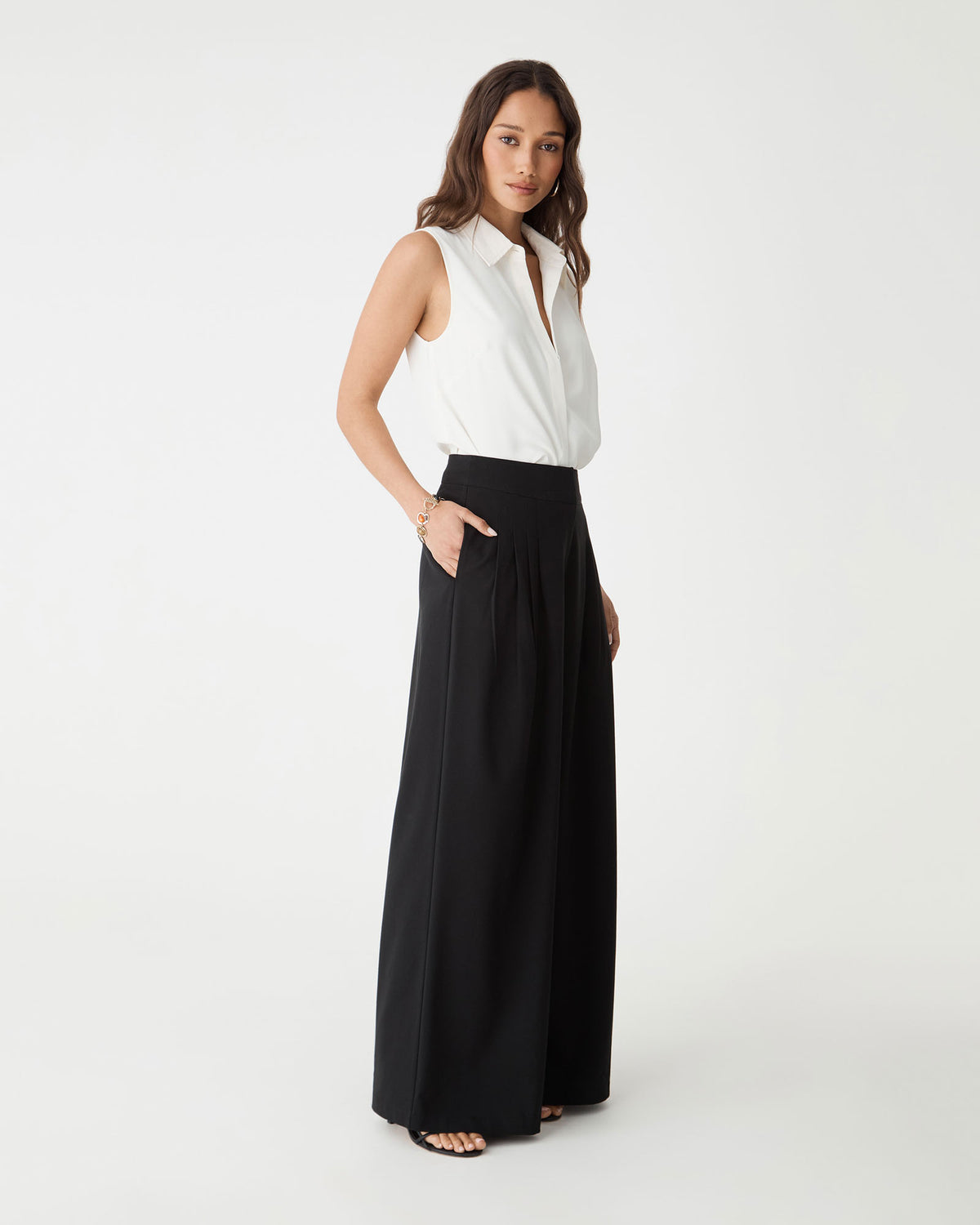 Side view of the ivory Brooklyn Sleeveless Shirt with black wide-leg trousers
