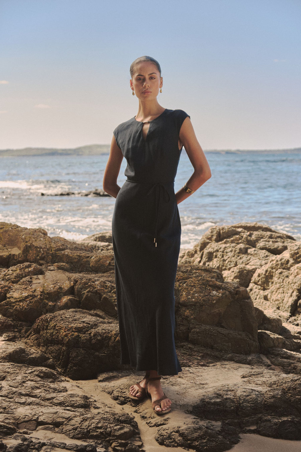 Phoebe Linen Blend Maxi Dress in navy, front view worn with self-tie waist belt on a rocky beach